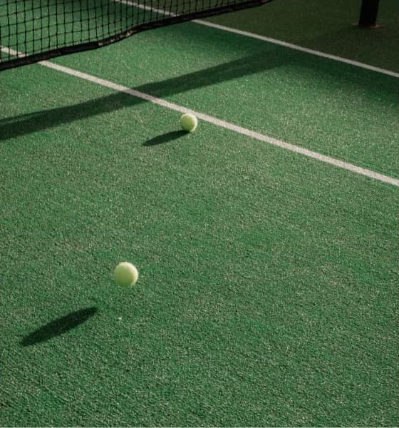 Two tennis balls bouncing beside a net on a green court
